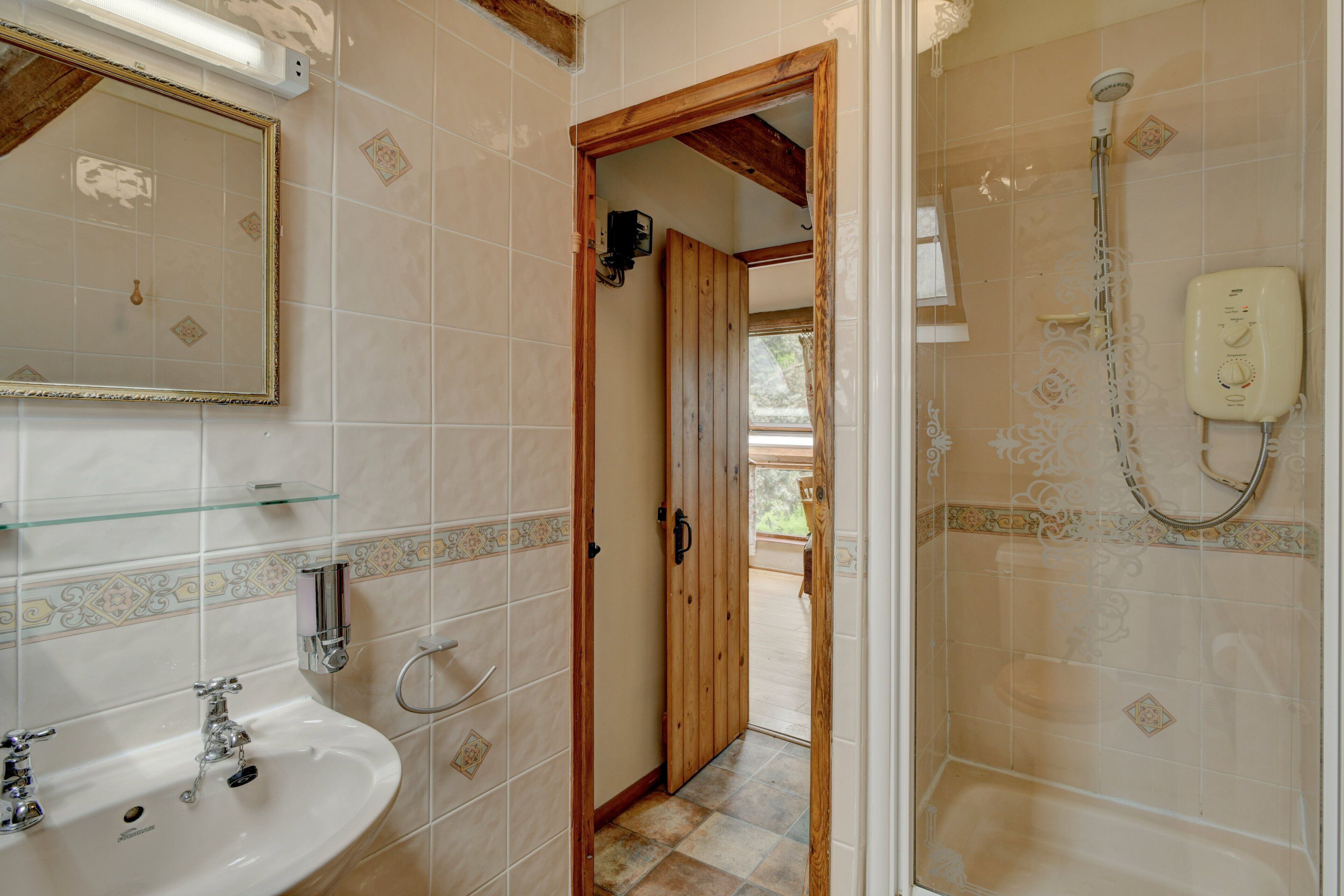 A bathroom with a sink, mirror, shower, and wooden door leading to another room.