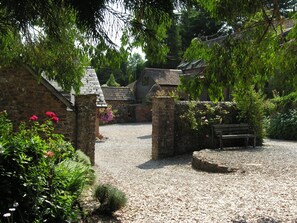 A stone building with a gravel path, a wooden bench, and a stone wall with flowers.