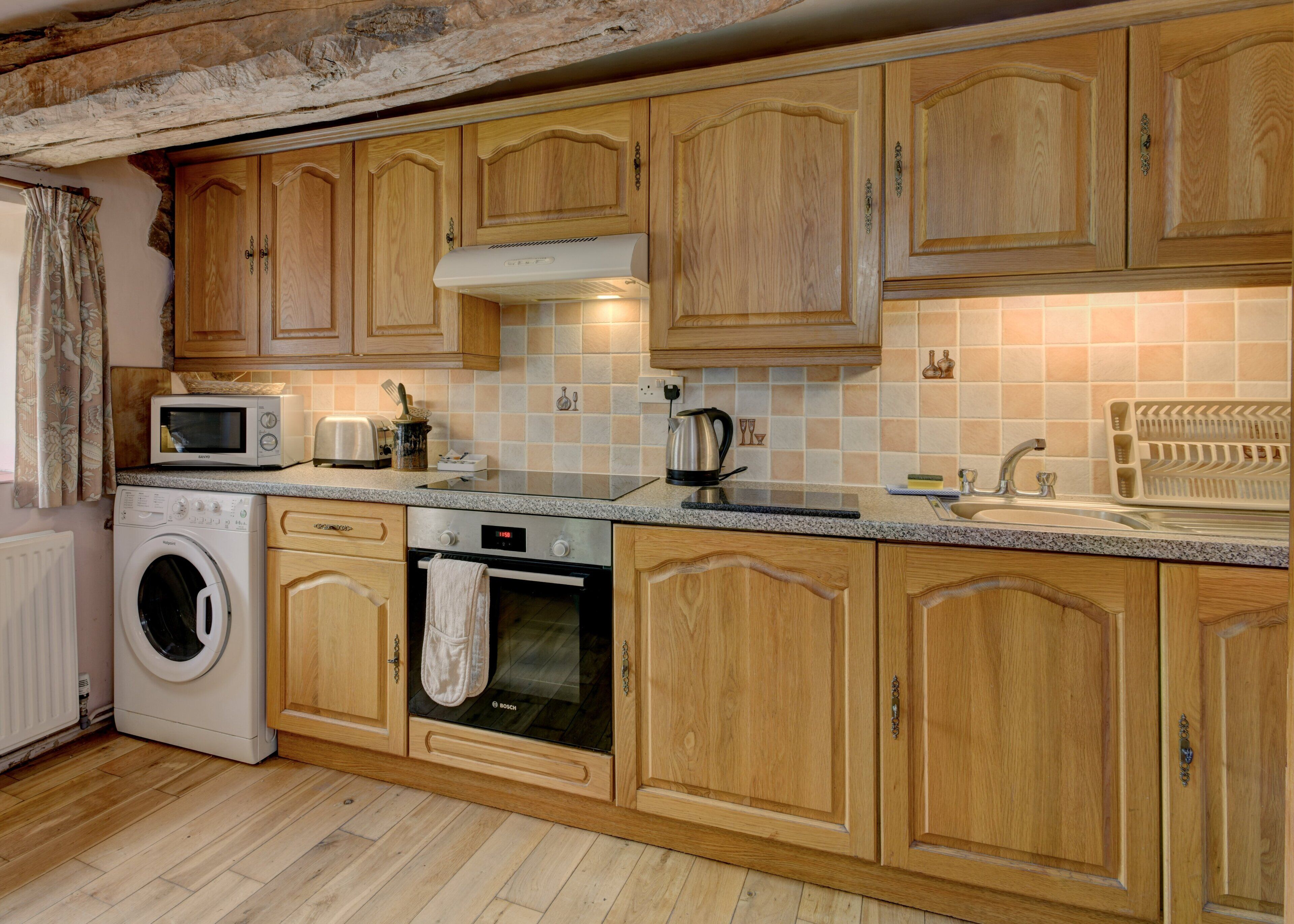 A kitchen with wooden cabinets, a washing machine, a microwave, a toaster, and a kettle.