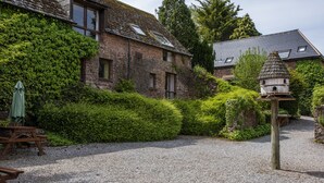 Ein Steinhaus mit efeuüberwachter Mauerwerk, eine Schotterauffahrt und ein Vogelhaus.