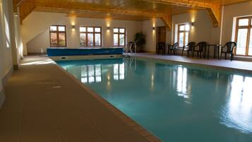Una piscina interna con una panchina, sedie e tavoli blu.