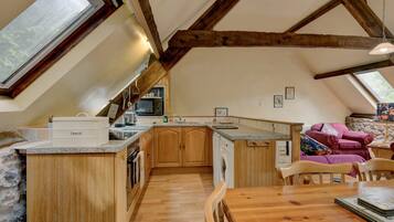 Een keuken met houten kastjes, een inbouwoven, een wasmachine en een eethoek met een houten tafel en stoelen.