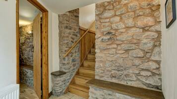 Una escalera de madera con paredes de piedra que conduce a una habitación con un radiador blanco y una puerta de madera.