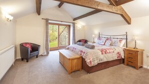 A bedroom with a large bed, wooden beams, a bench, a chair, and a view through a window. - Red Deer Cottage, Wheddon Cross (Wheddon Cross)
