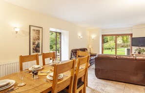 A dining area with a wooden table set for four, a brown leather sofa, and a TV mounted on the wall.