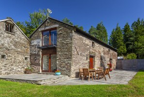 Un bâtiment en pierre doté d’un balcon, une terrasse avec une table et des chaises, et un jardin.