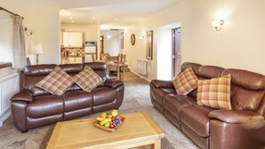 A living room with two brown leather sofas, a wooden coffee table with fruit, and a kitchen in the background. - Red Deer Cottage, Wheddon Cross (Wheddon Cross)