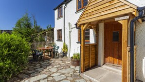 A stone-paved patio with a wooden table and chairs, a wooden door labeled 'Hedgehog,' and a white building with multiple windows. - Hedgehog Cottage, Wheddon Cross (Wheddon Cross)