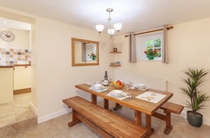 A dining area with a wooden table set for four, a bench, a mirror, a window with curtains, and a potted plant.