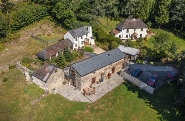A large estate with multiple buildings, a stone house, and a paved driveway with parked cars.