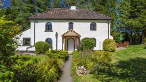 A white building with a tiled roof, a central entrance with an arch, and a paved pathway leading to the entrance. - Barn Owl Cottage, Wheddon Cross (Wheddon Cross)