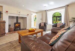 A living room with a fireplace, leather sofa, wooden coffee table, and a view of greenery outside.