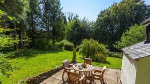 A patio with a table and chairs, surrounded by a lush garden and trees. - Barn Owl Cottage, Wheddon Cross (Wheddon Cross)