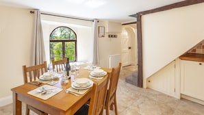A dining area with a wooden table set for four, a window with a view of greenery, and a staircase leading to an upper level. - Barn Owl Cottage, Wheddon Cross (Wheddon Cross)