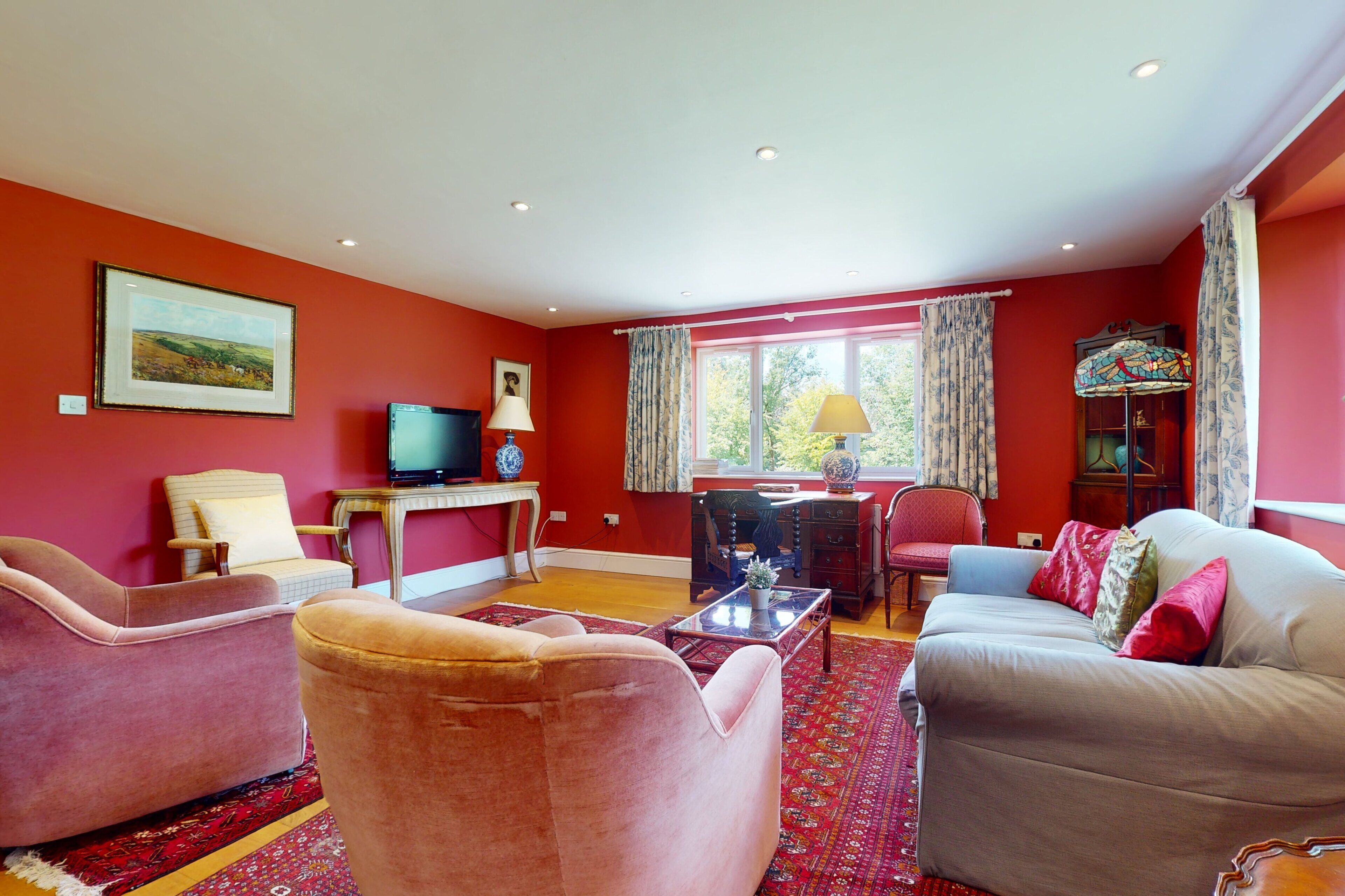 A living room with a red wall, a television, a table with a lamp, a sofa, and a window with curtains.