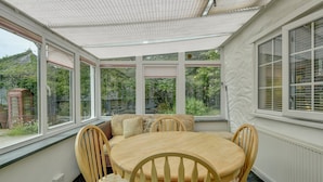 A sunlit room with a round wooden table and chairs, large windows, and a view of greenery outside. - Hartford Cottage, West Anstey (West Anstey)