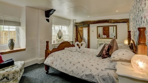 A bedroom with a wooden bed, a bedside table, a mirror, and a window with blinds. - Hartford Cottage, West Anstey (West Anstey)