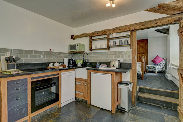 A compact kitchen with a microwave, oven, and dishwasher, wooden cabinets, and a small refrigerator.