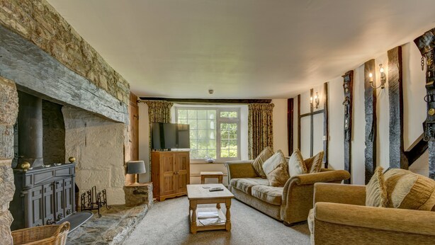 A cozy living room with a stone fireplace, a television, a sofa, and a coffee table. - The Farmhouse, West Anstey (West Anstey)