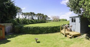 A small wooden shed with a deck, a fenced garden area with a hedge, and a bird bath.