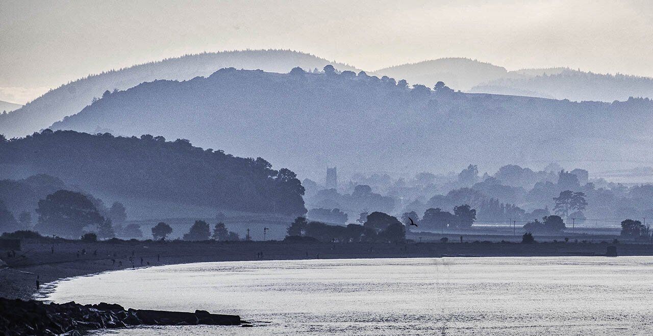 Un paysage côtier avec une rivière, des collines et un bâtiment situé au loin.