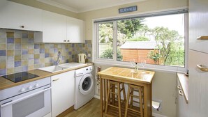 A compact kitchen with a washing machine, a wooden table, and a window with a view of greenery. - Pine in Cleeve Park Near Blue Anchor (Near Blue Anchor)