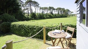 A wooden deck with a table and chairs, surrounded by a rope barrier and a hedge. - Pine in Cleeve Park Near Blue Anchor (Near Blue Anchor)