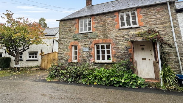 A stone cottage with a white door, a small porch, and a sign reading "Riverside Cottage." - Riverside Cottage, Brendon (Nr Lynton)
