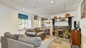 A living room with a fireplace, sofas, and a stone fireplace surround. - Riverside Cottage, Brendon (Nr Lynton)