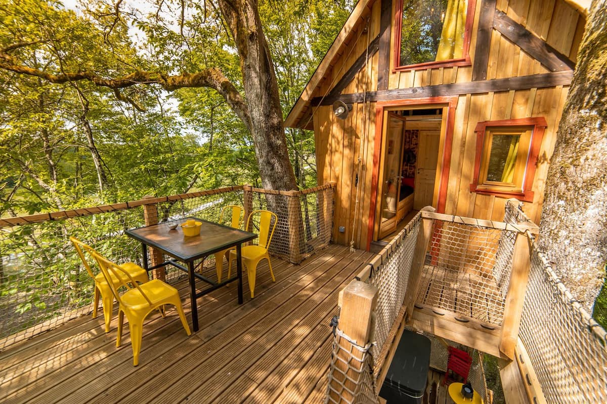 Una cabana de fusta amb terrassa, cadires grogues i una taula.