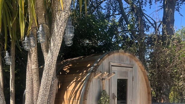 A wooden barrel-shaped structure with a door, surrounded by white pebbles and a tiled floor. - Stables Cottage, Ellicombe (Minehead)