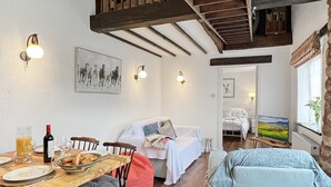 A cozy room with a wooden dining table set for breakfast, a bed with a white duvet, and a painting on the wall. - Stables Cottage, Ellicombe (Minehead)