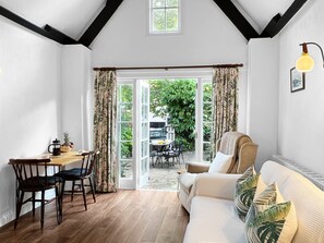 Une pièce chaleureuse avec un plancher en bois, une table à manger avec des chaises, un canapé avec des coussins et une grande fenêtre avec des rideaux.