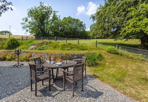 An outdoor seating area with a round table and chairs, surrounded by a gravel path and a stone wall.
