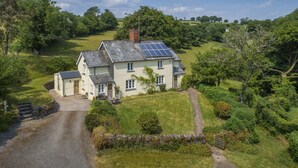 Une grande maison à deux étages, avec une allée pavée et un petit garage séparé.