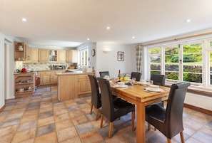 A modern kitchen with wooden cabinets, a dining table with chairs, and a large window with a view of greenery.