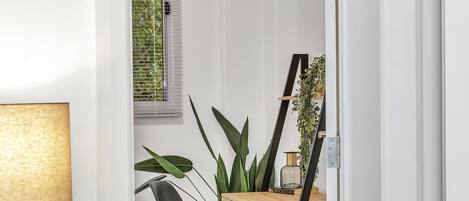 Um espaço de trabalho compacto com uma secretária de madeira, uma cadeira preta, uma lâmpada e uma planta em vaso.