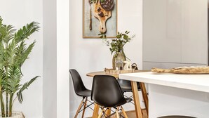 A dining area with a white table, black chairs, a wooden cutting board with a bowl and spoon, and a vase with flowers. - Glenelg Stay at The Bay (Glenelg South)