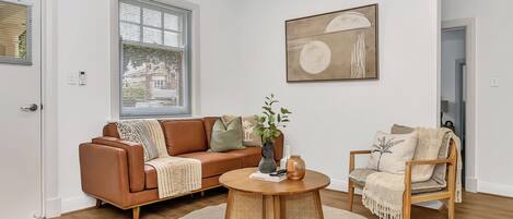 A modern living room with a brown leather sofa, a wooden coffee table, and a beige armchair.