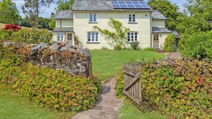 A two-story house with a garden, a stone wall, and a wooden gate. - One Lower Spire Cottage, Liscombe (Nr Dulverton)