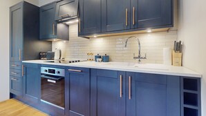 A modern kitchen with dark blue cabinets, a white countertop, a built-in oven, and a stainless steel sink.