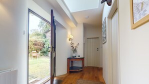 A hallway with wooden flooring, a glass door leading to a garden, a small table with a vase, and a framed picture on the wall.