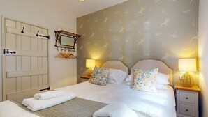 A neatly made bed with pillows and a blanket, a bedside lamp, a small wooden nightstand, and a wall-mounted mirror.