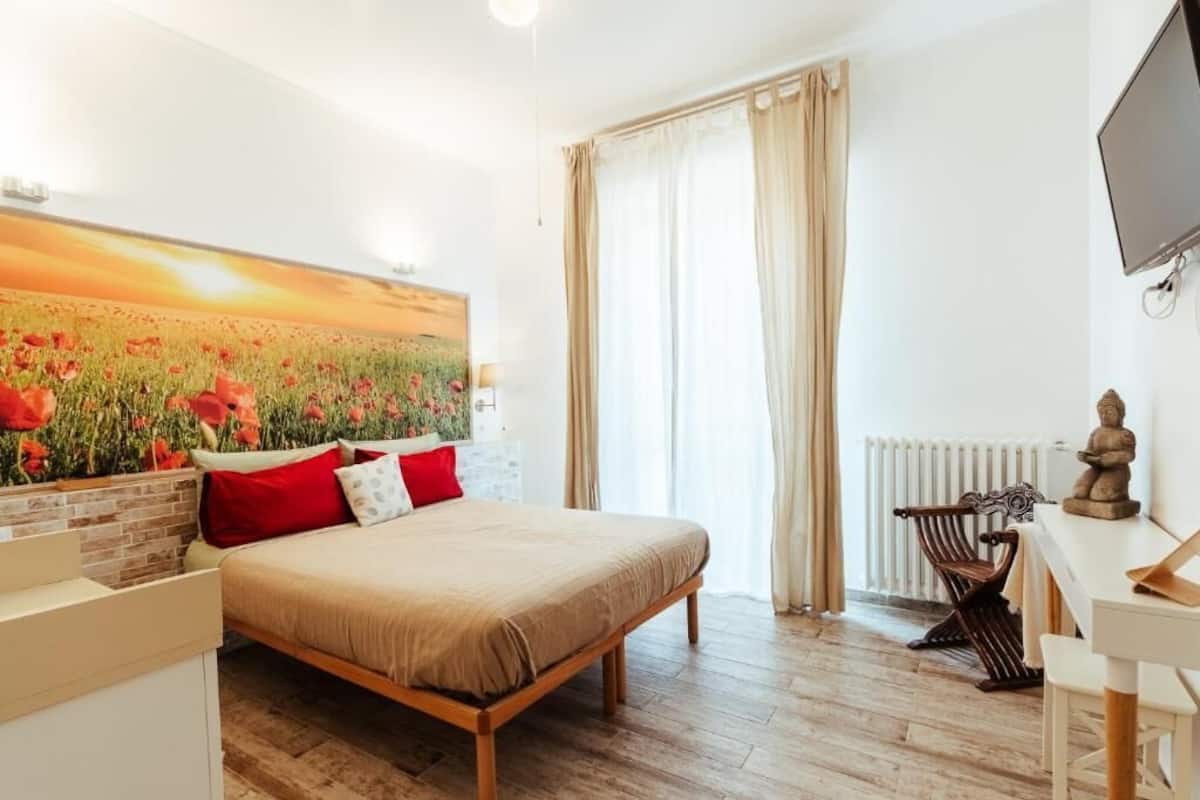 A bedroom with a bed, a desk, a chair, a radiator, and a TV.