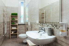 Une salle de bain moderne avec un lavabo blanc, des toilettes, un porte-serviettes et une étagère avec des serviettes.