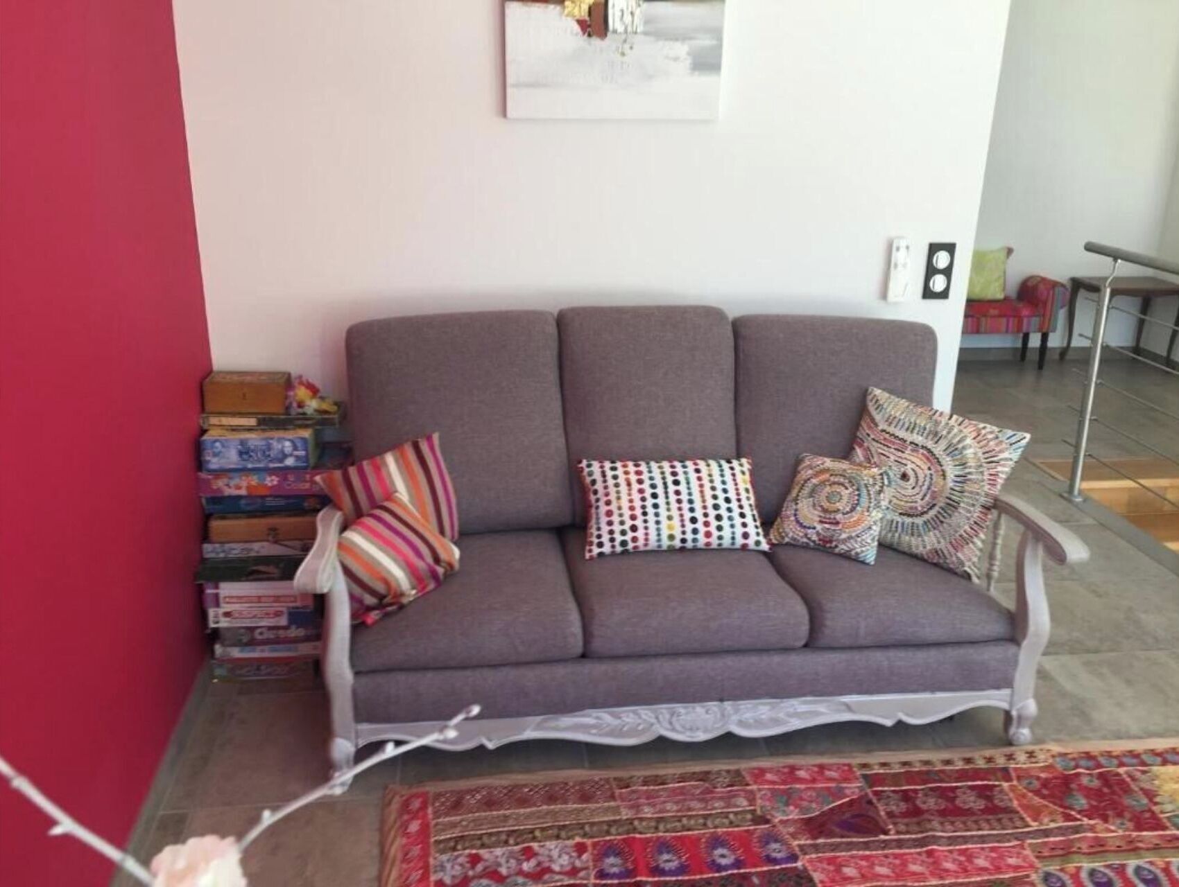 A living room with a grey sofa, colorful pillows, a stack of books, and a patterned rug.