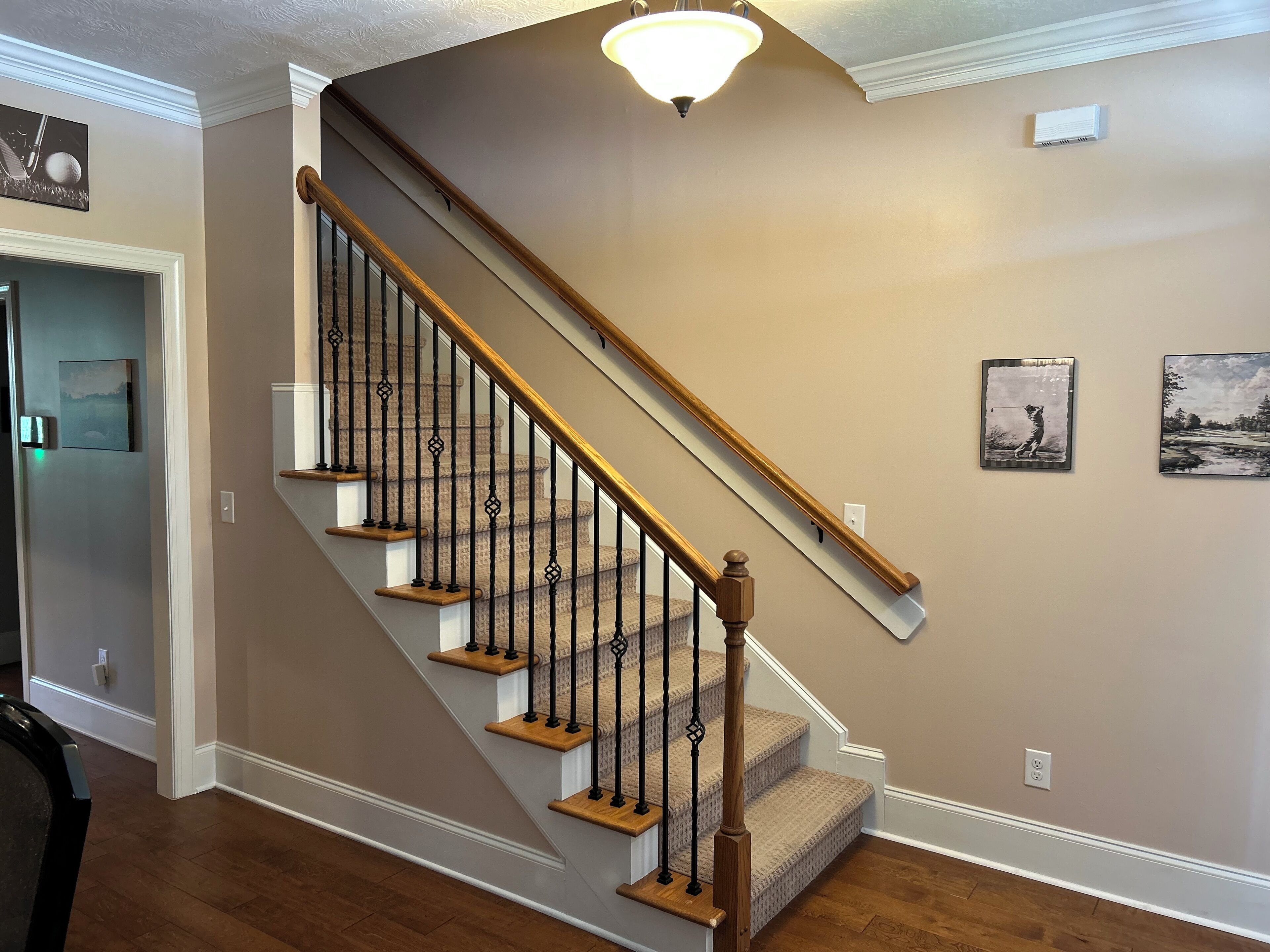Un escalier avec des marches en bois et des balustrades noires, un luminaire au-dessus et deux tableaux encadrés accrochés au mur.