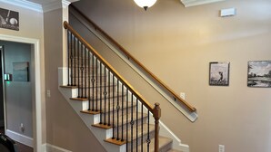 Een trap met houten treden en zwarte balustrades, een lamp erboven en twee ingelijste foto's aan de muur.