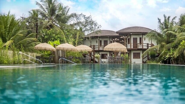 A resort with a swimming pool, thatched umbrellas, and tropical vegetation. - Hotel Villa Balidendê (Maraú)