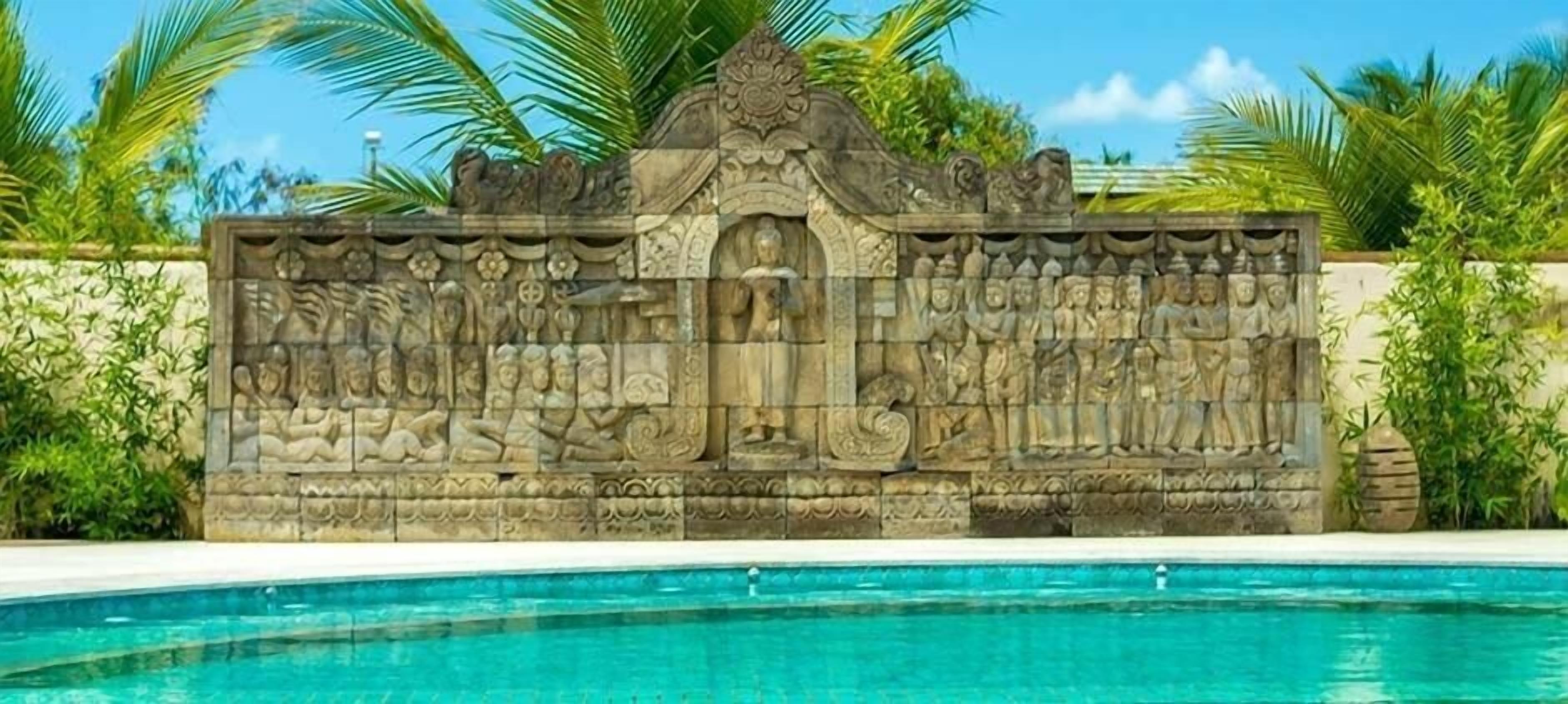 A stone wall with intricate carvings and a pool in the foreground.